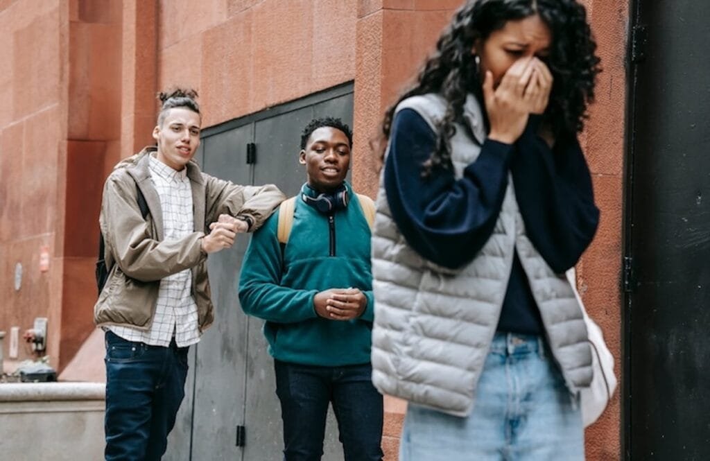 Girl being bullied by two boys who are laughing behind her. Social anxiety hypnosis London.