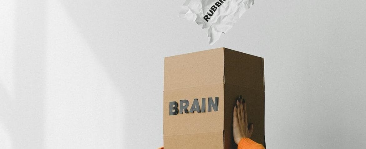 Image of a woman wearing a box on her head that is labelled brain, and a man pouring rubbish into it. Hypnotherapy London with Rowenna