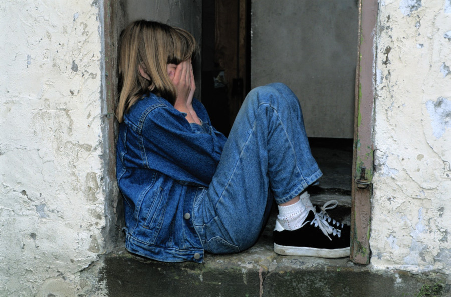 Image of a young girl sitting alone in a doorway with her head in her hands, low self-esteem hypnotherapy with Rowenna