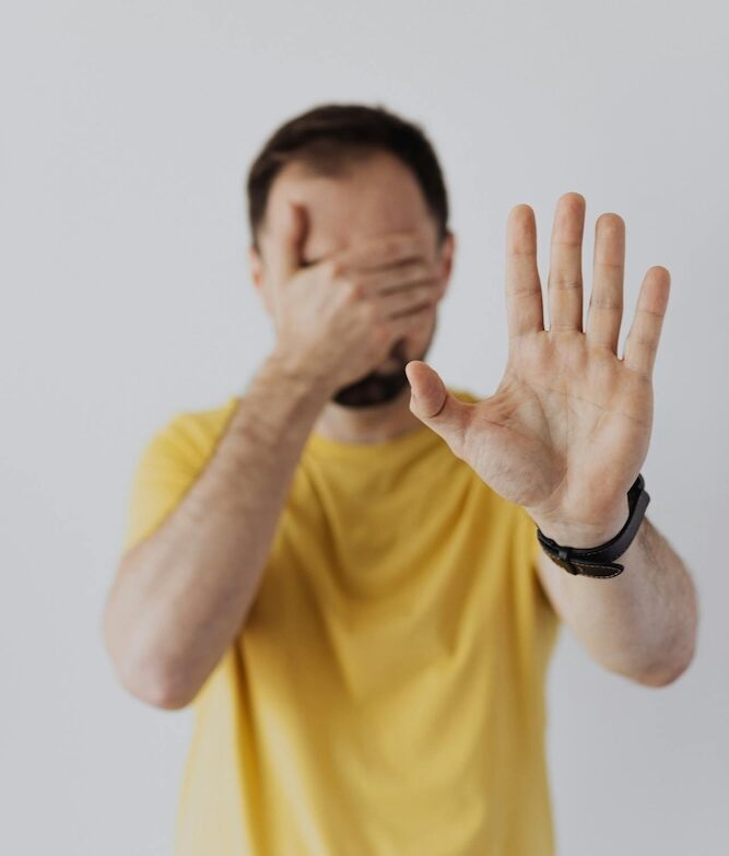 Image of a man holding one hand over his eyes and one hand up in front of him to suggest no, avoidant attachment hypnotherapy with Rowenna
