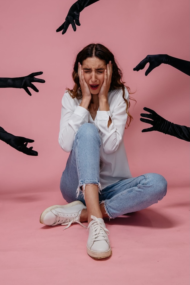 Image of a woman sitting on the floor looking scared while shadow hands reach for her, social anxiety hypnotherapy and CPTSD support group online