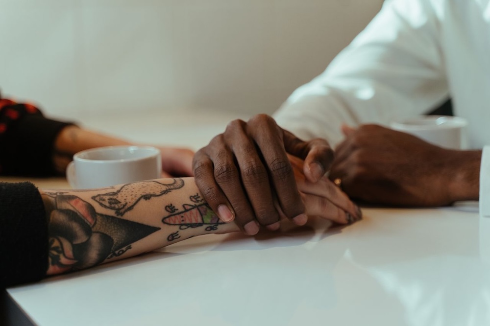 Image of two people holding hands across a table, connection is possible for survivors of trauma