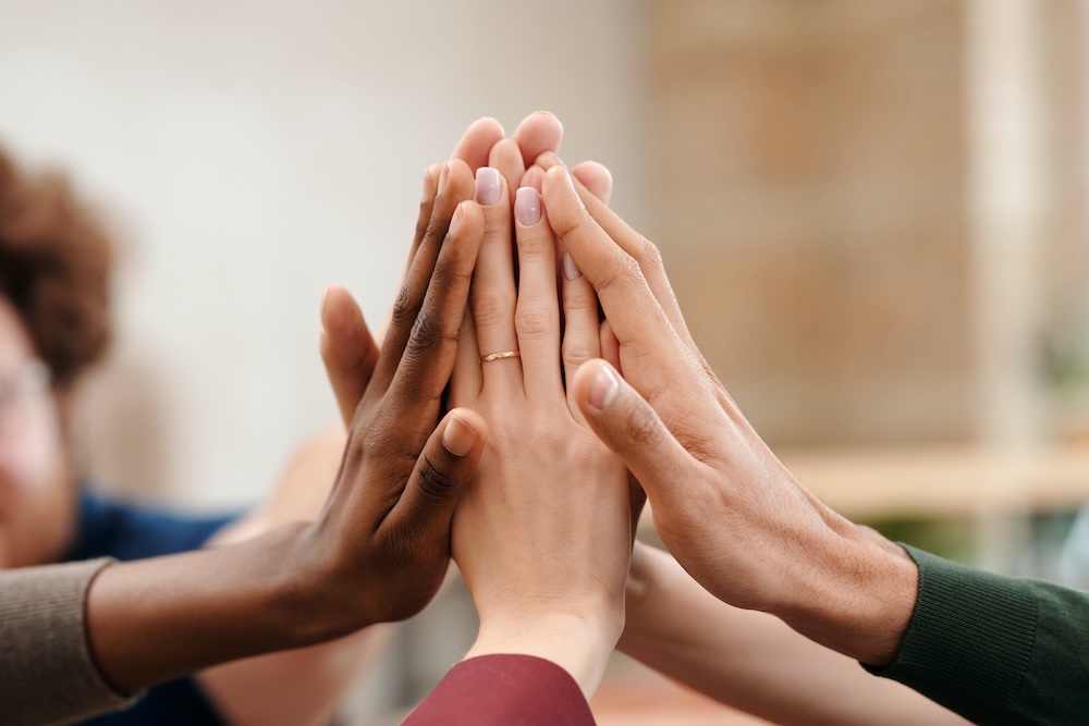 Image of a group of people's hands in a joined hi five, online CPTSD support group with Rowenna
