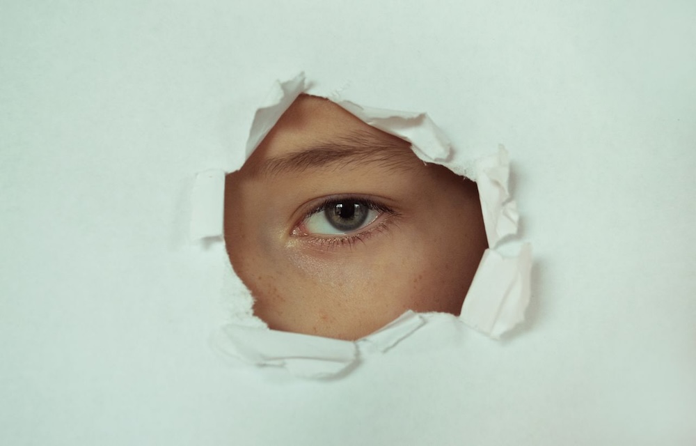 Image of a hole in a piece of paper with an eye peering through, hidden shame, complex trauma and vulnerability blog