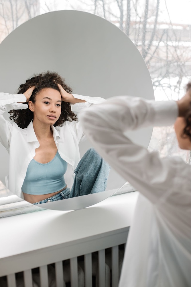 Image of a woman looking into a mirror and feeling stressed about her looks, self-esteem hypnotherapy with Rowenna