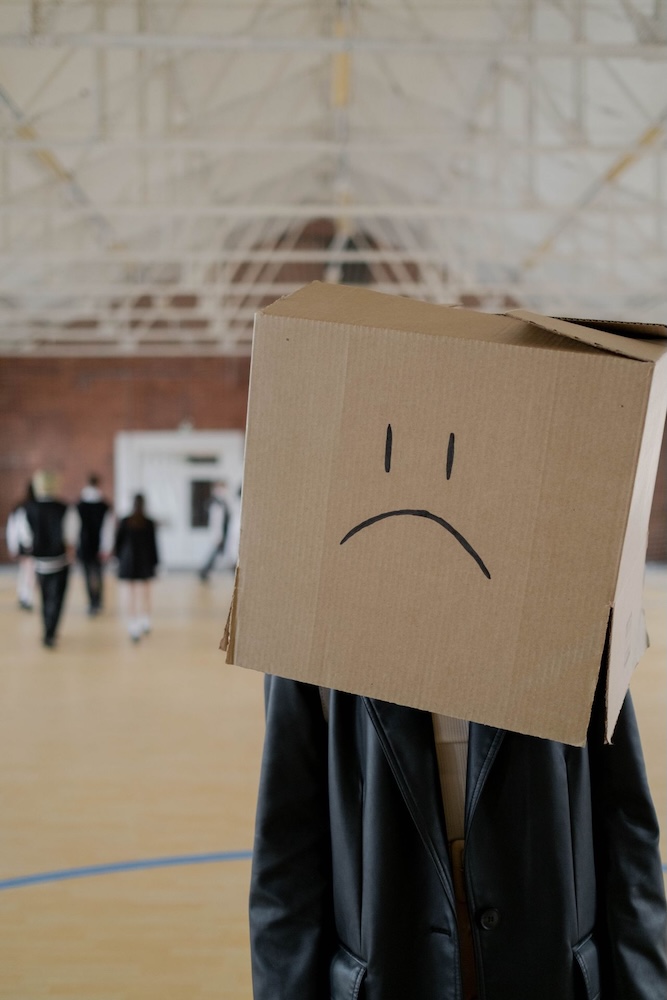 Image of a person wearing a box over their head with a sad face drawn on it, social anxiety hypnotherapy with Rowenna