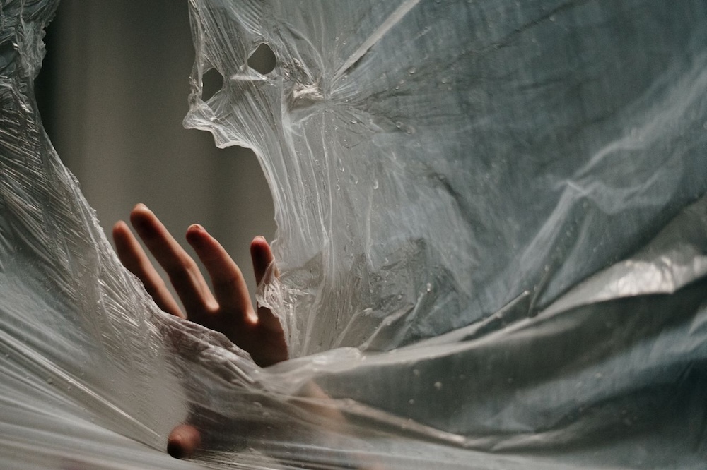 Image of a woman's hand breaking through a plastic sheet, complex trauma and vulnerability blog by Rowenna Clifford