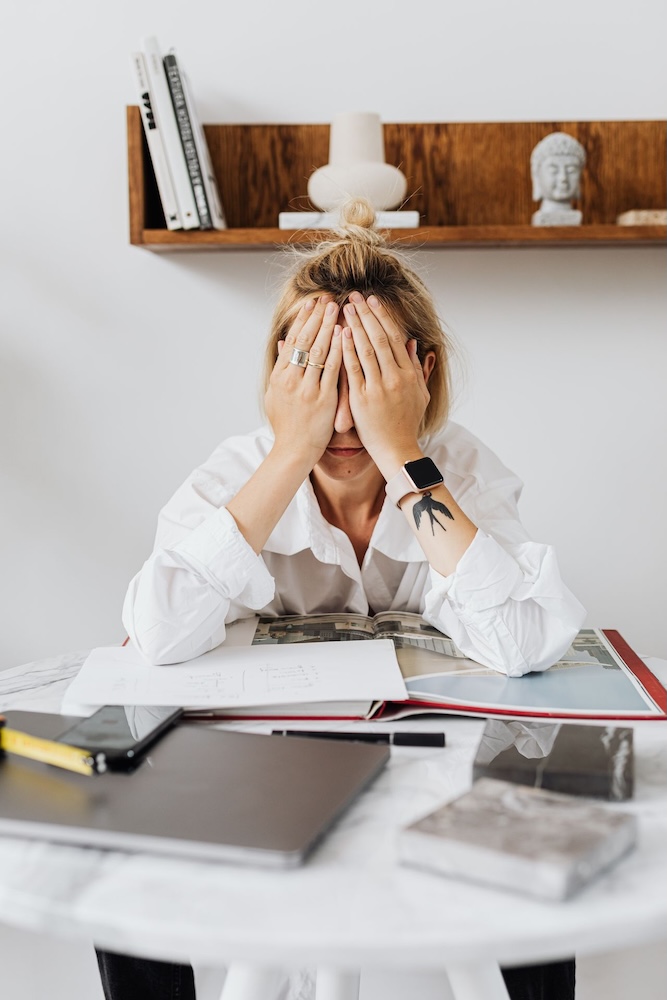 Image of a woman at her desk with her head in her hands, imposter syndrome hypnosis with Rowenna
