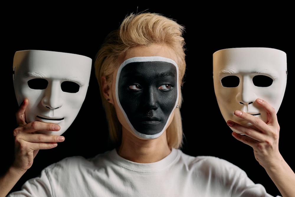 Image of a woman holding two masks up, imposter syndrome hypnosis with Rowenna