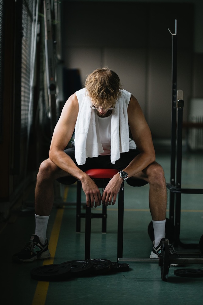 Image of a man sitting in the locker rooms with his head down, performance anxiety hypnotherapy with Rowenna