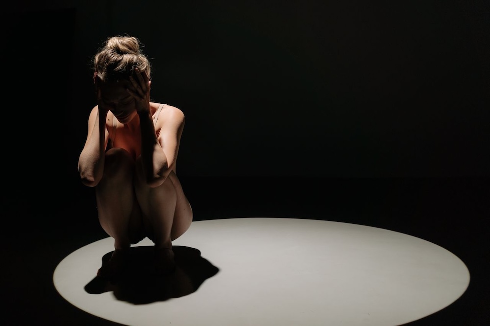 Image of a woman under a spotlight, she's crouching down with her head in her hands, performance anxiety hypnotherapy with Rowenna