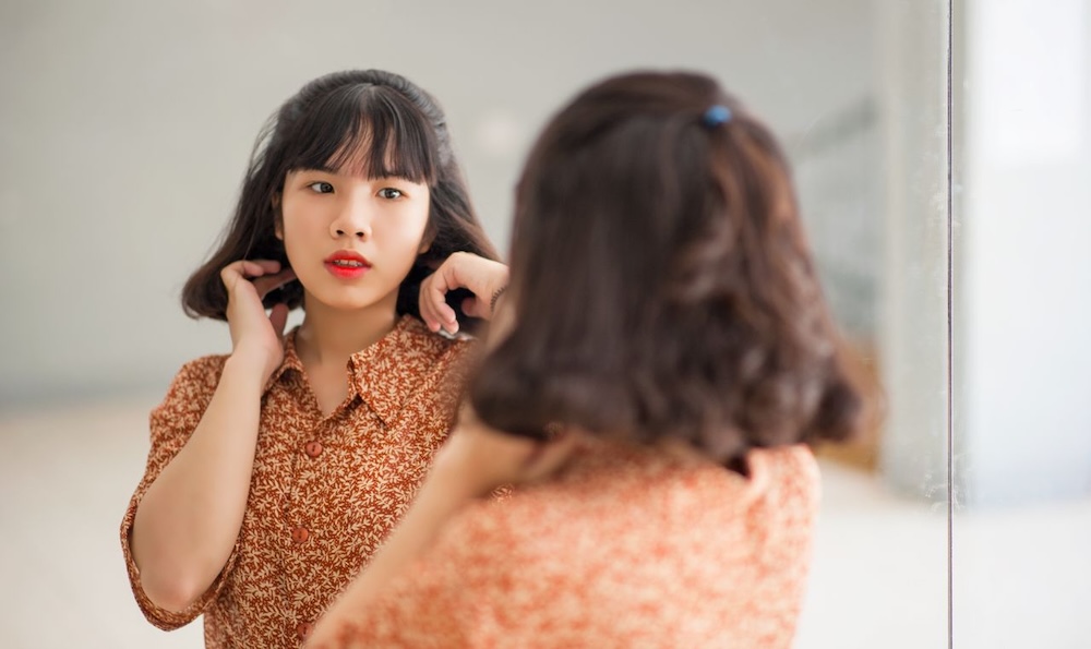 Image of a woman looking at herself in the mirror looking sad, how childhood attachment can lead to low self esteem