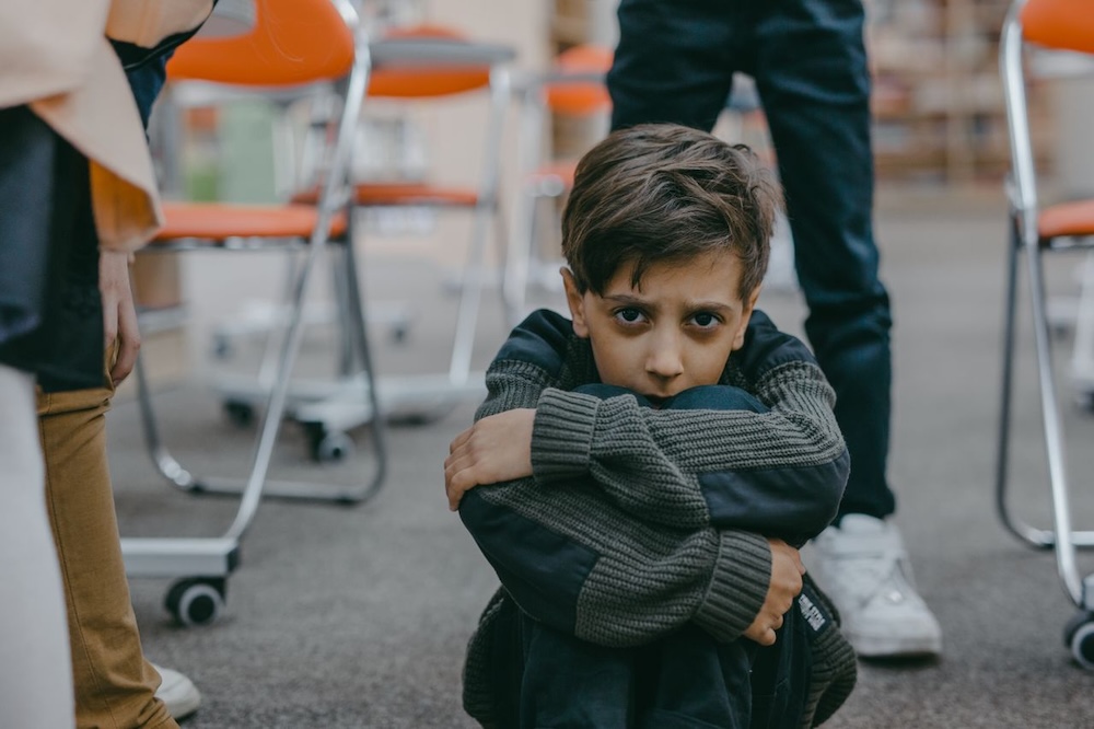 Image of a boy sitting on the floor at school, looking scared and shy, what causes low self esteem blog by Rowenna Clifford Hypnotherapy