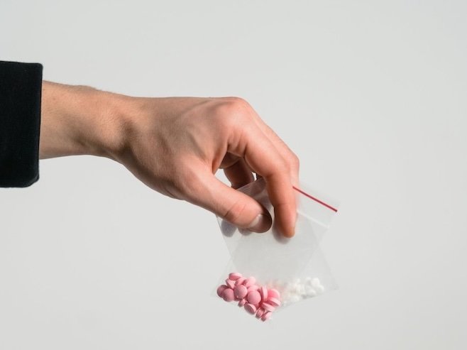 Image of a man's hand holding a zip lock bag with pills in it, addiction hypnotherapy london with Rowenna Clifford